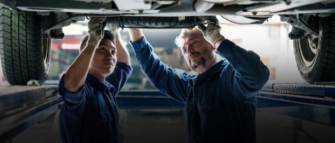 Two mechanics examining a vehicle from underneath