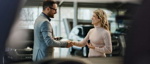 Man shaking hands with a woman holding a key to a new car.